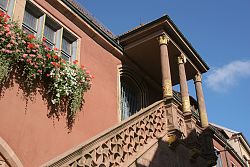 Das Bild zeigt die Außentreppe an der rechten Seite des  Alten Rathauses. Vor den Fenster in ersten Stock hängen Blumen.